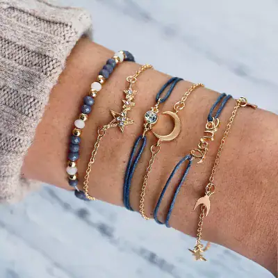 Brass gold-tone moon, star, and dolphin charms with blue cord and bead bracelets, perfect for women's fashion; stylish and trendy jewelry accessories.