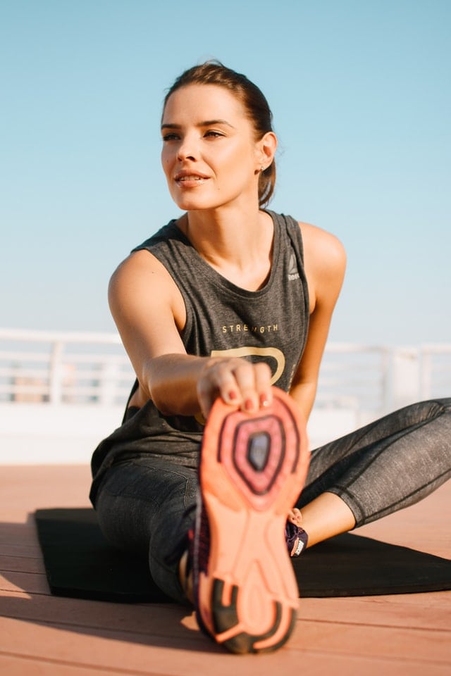Young woman stretching outdoors, practicing yoga for flexibility and health, wearing sportswear, with clear blue sky background.