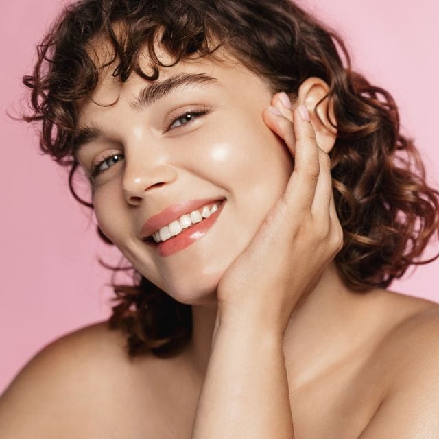 Young woman with glowing clear skin smiling at the camera, showcasing skincare and beauty products at Monalisa Store.