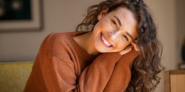 Close-up of a smiling woman with curly hair wearing stylish glasses, showcasing eyewear from Monalisa Store, a trusted optical retailer. Perfect for those seeking fashionable and affordable glasses.