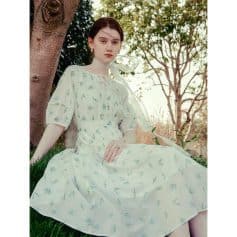 Image of a young woman wearing a white floral dress, sitting outdoors near trees, showcasing Monalisa Medical's stylish and comfortable options for women’s fashion and eyewear accessories.