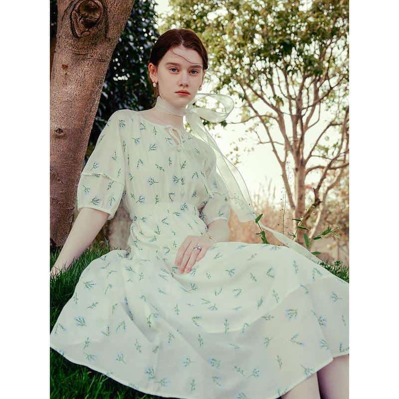 Image of a young woman wearing a white floral dress, sitting outdoors near trees, showcasing Monalisa Medical's stylish and comfortable options for women’s fashion and eyewear accessories.