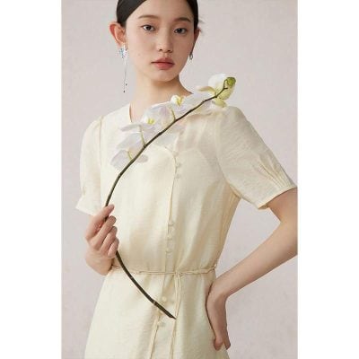 Close-up of a woman wearing a stylish cream-colored dress holding a white orchid flower, emphasizing fashion and beauty, ideal for promotional images of Monalisa Medical Store's fashion accessories and elegant apparel.