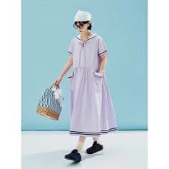 A woman in a stylish, lavender casual dress with black trim, accessorized with jewelry, glasses, and a white cap, carrying a striped bag. Perfect for summer outings, showcasing trendy women's fashion from Monalisa Medical store.