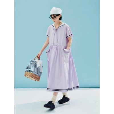 A woman in a stylish, lavender casual dress with black trim, accessorized with jewelry, glasses, and a white cap, carrying a striped bag. Perfect for summer outings, showcasing trendy women's fashion from Monalisa Medical store.