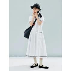 Image of a young woman wearing a fashionable white dress with black accents, accessorized with a black wide-brimmed hat, black shoes, and a black shoulder bag, embodying trendy summer fashion.