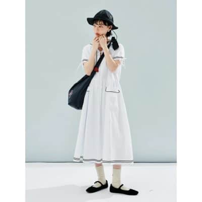 Image of a young woman wearing a fashionable white dress with black accents, accessorized with a black wide-brimmed hat, black shoes, and a black shoulder bag, embodying trendy summer fashion.