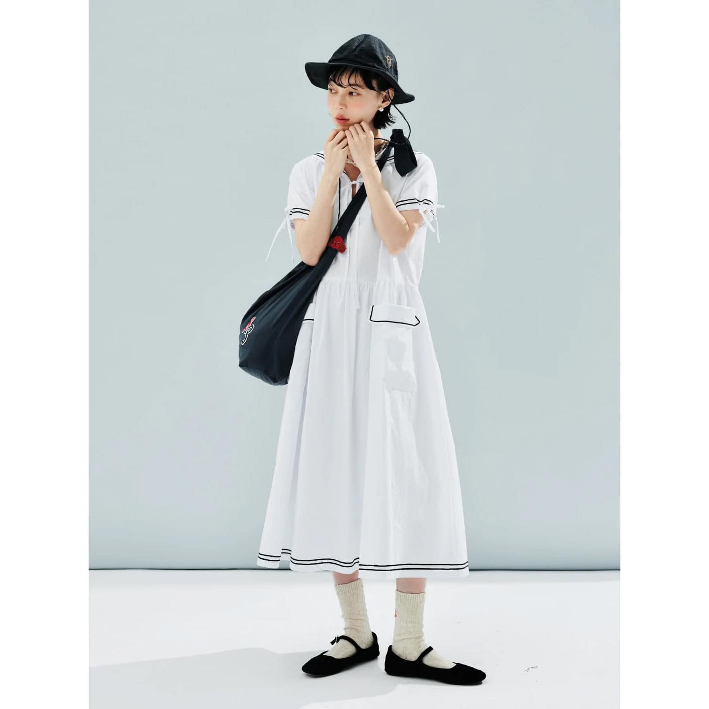 Image of a young woman wearing a fashionable white dress with black accents, accessorized with a black wide-brimmed hat, black shoes, and a black shoulder bag, embodying trendy summer fashion.