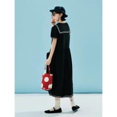 Stylish young woman wearing a black dress with sailor collar, black hat, glasses, and carrying a red polka dot tote bag, showcasing trendy accessories and apparel at the Monalisa medical fashion store.