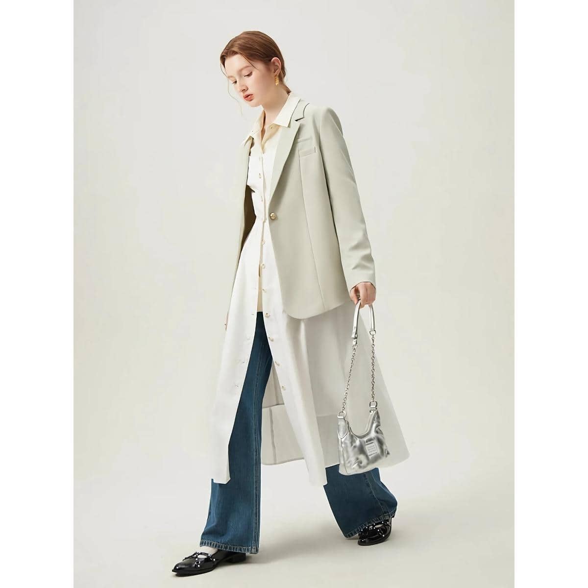 Elegant women's outfit featuring a beige blazer over a long shirt, paired with flared jeans and stylish shoes, showcasing modern fashion and accessories for a sophisticated look.