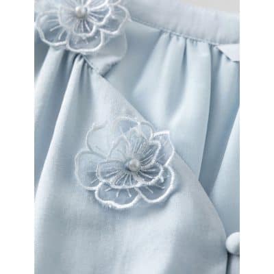 Close-up of a light blue silk garment featuring floral embroidery with pearl details for a sophisticated look.