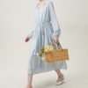 Stylish woman in a flowing light blue dress holding a woven basket with flowers, showcasing exclusive fashion options at Monalisa Store for summer and casual wear.