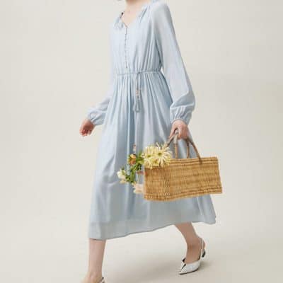 Stylish woman in a flowing light blue dress holding a woven basket with flowers, showcasing exclusive fashion options at Monalisa Store for summer and casual wear.