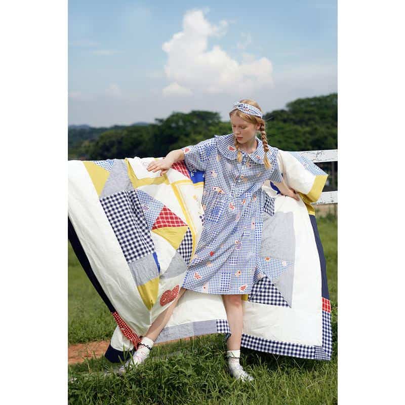 Bright and colorful girl wearing patchwork dress with optical frames in natural outdoor setting.