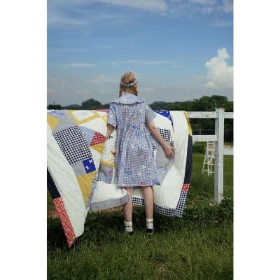Adorable girl hanging quilt outdoors, rural setting, bright sky, nostalgic and charming scene.