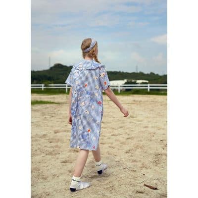 Child girl wearing a playful, patterned dress with matching headband outdoors, showcasing stylish kids' fashion and comfortable summer apparel for children.