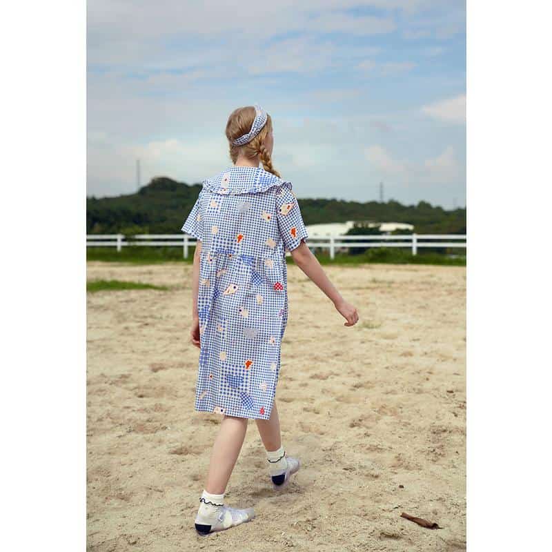 Child girl wearing a playful, patterned dress with matching headband outdoors, showcasing stylish kids' fashion and comfortable summer apparel for children.