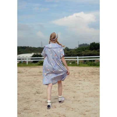 Child girl wearing a stylish gingham dress with floral print, perfect for summer outdoor activities. Comfortable and trendy choice for children’s fashion.