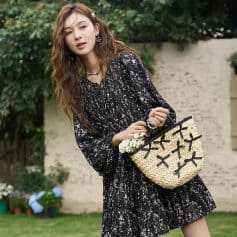 Stylish woman holding a woven handbag featuring black ribbon bows, wearing a chic black and white printed dress, perfect for fashion-forward outings and accessories shopping.