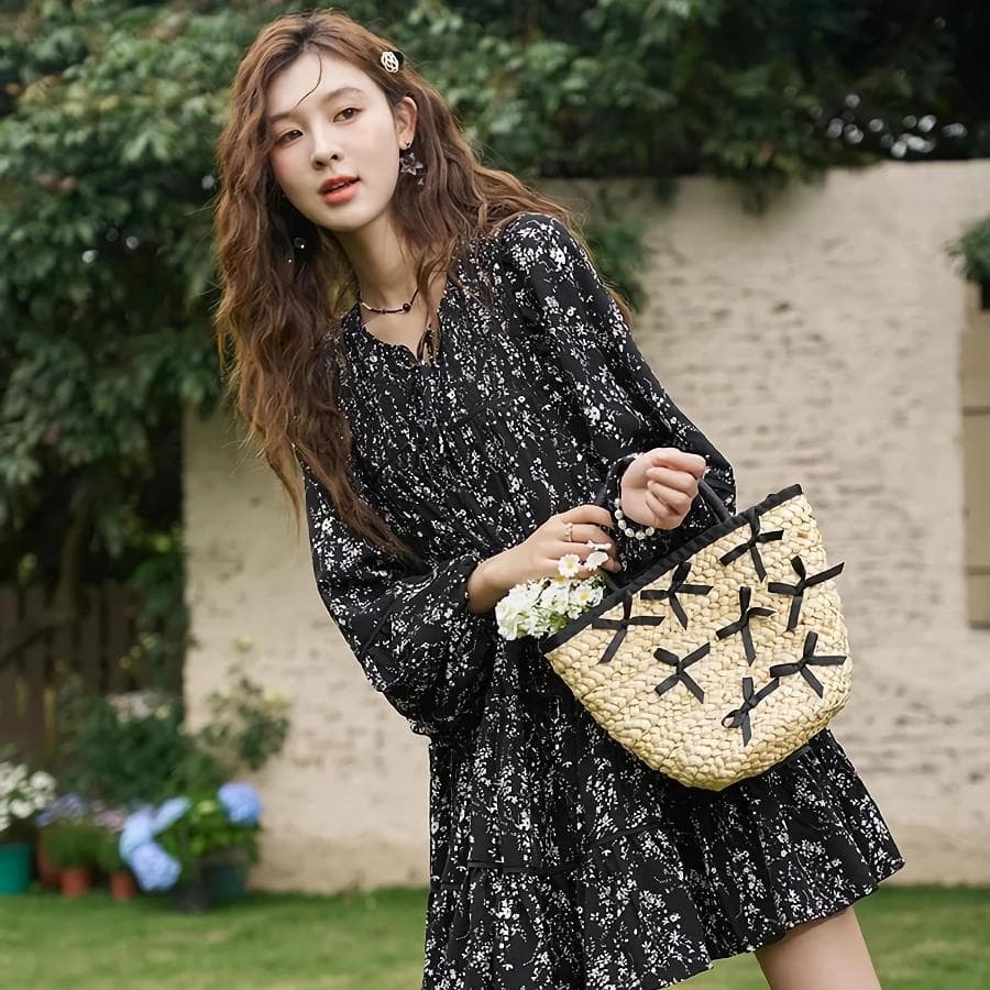 Stylish woman holding a woven handbag featuring black ribbon bows, wearing a chic black and white printed dress, perfect for fashion-forward outings and accessories shopping.