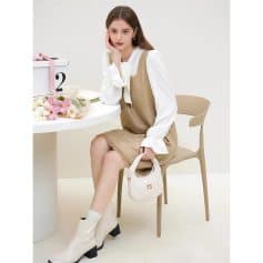 A stylish woman sits at a minimalistic table with flowers, a white gift box, and a beige Miu Miu handbag, showcasing contemporary fashion and accessories for women.