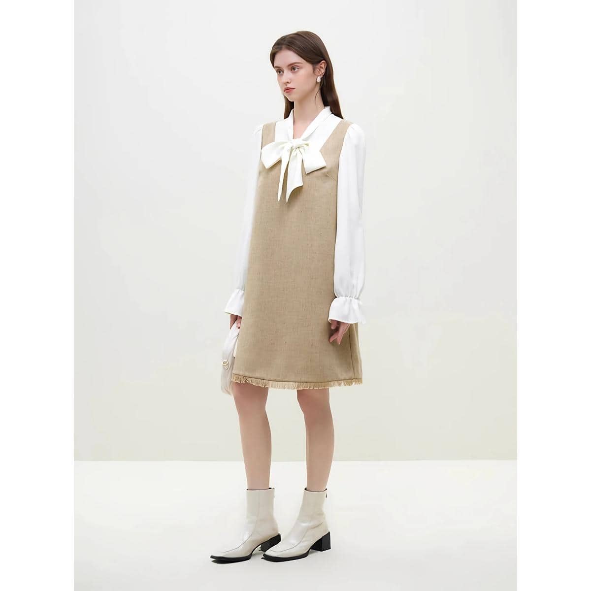 A fashionable model showcases a beige dress layered over a white blouse with a bow tie, complemented by white ankle boots. The outfit exudes elegance and modern style, emphasizing comfort and sophistication. Perfect for fashion-forward women looking for versatile, trendy apparel available at Monalisa Store.
