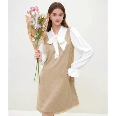A stylish beige dress layered over a white blouse with puffed sleeves and a bow tie accent, perfect for professional or formal events, featuring a knee-length design and refined details.