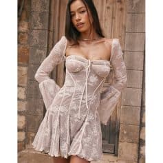 A woman wearing a stylish, sheer lace dress with puffed sleeves and a front tie detail, perfect for upscale occasions or fashion forward events.