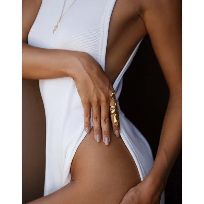 Close-up of a woman wearing a stylish white dress, showcasing gold snake rings on her hand, perfect for fashion and jewelry lovers.