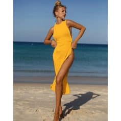 A woman in a stylish yellow beach cover-up dress walking on the sandy shore with ocean backdrop, perfect for summer beach fashion and swimwear cover-ups.