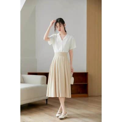 A stylish woman in a sophisticated white blouse and beige pleated midi skirt, showcasing elegant and professional fashion ideal for workplace and formal occasions.