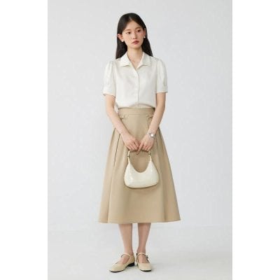 Elegant woman with beige skirt and white blouse holding a stylish cream handbag.