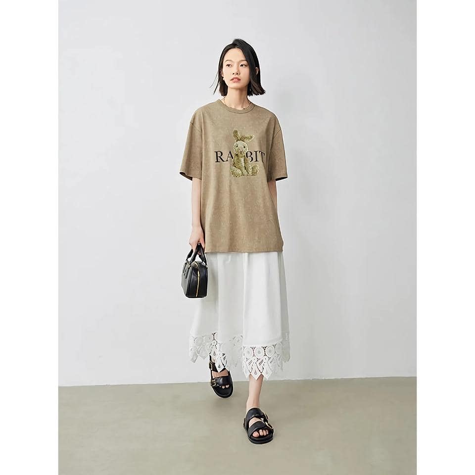 Comfortable women's fashion featuring a beige T-shirt with a rabbit graphic and "RABBIT" text, paired with a white lace-trimmed skirt, stylish sandals, and a black handbag, perfect for everyday or casual outings.