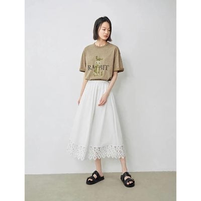 Stylish girl wearing a beige graphic T-shirt with "RABBIT" text and bunny illustration, paired with a white eyelet lace hem midi skirt and black sandals. Perfect for trendy, casual outfits.