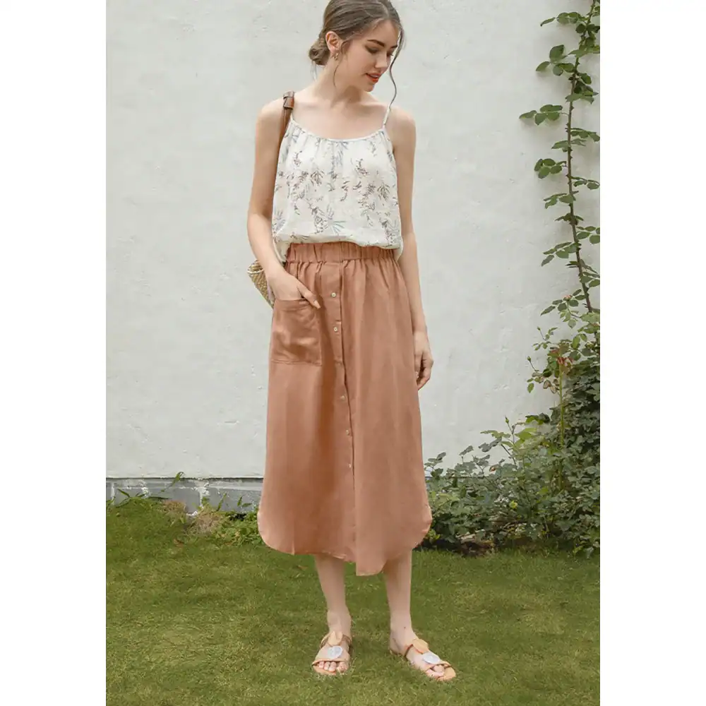 Young woman wearing a floral top and tan satin skirt in a garden setting, showcasing trendy women's fashion for casual and everyday wear.