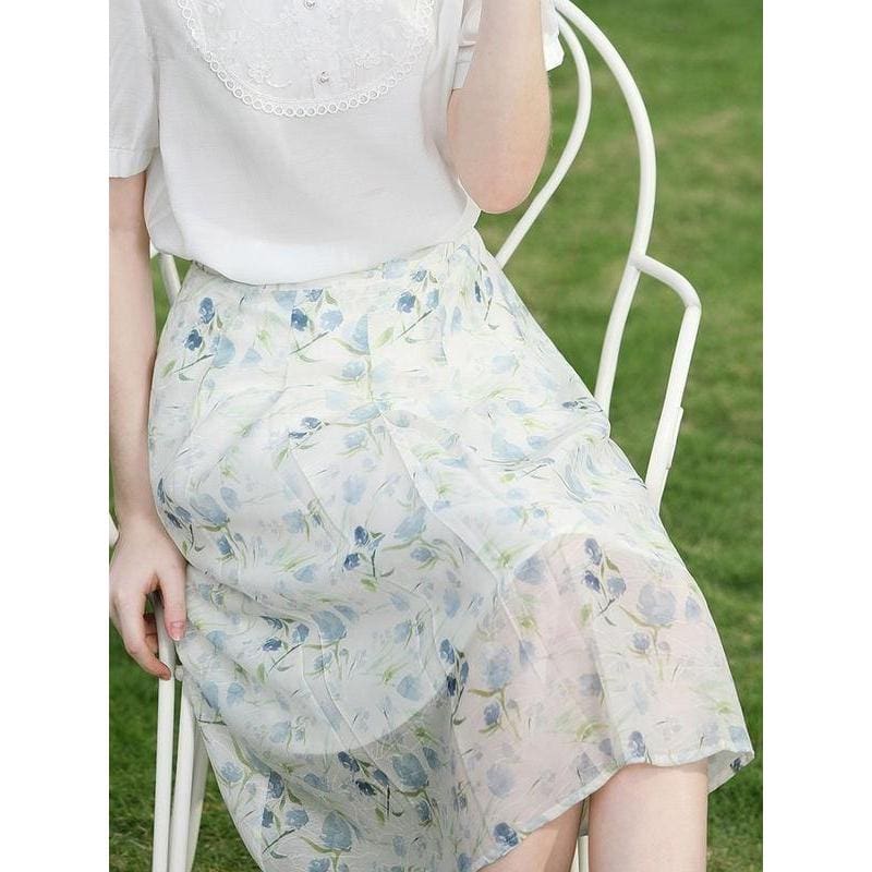 A woman wearing a delicate floral skirt seated on a white garden bench outdoors, showcasing feminine and stylish summer clothing from Monalisa Medical. The light, airy fabric and floral pattern highlight comfort and elegance in an outdoor setting. Perfect for casual and garden wear, emphasizing fashion, comfort, and summer style.