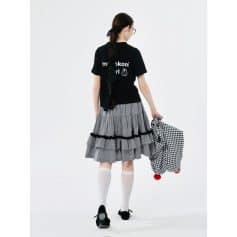 Young girl with long hair, glasses, and school bag, dressed in stylish skirt and black T-shirt, walking away.