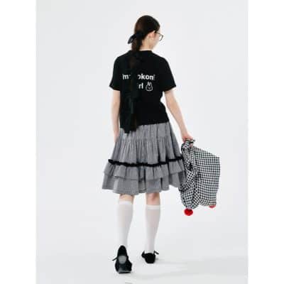 Young girl with long hair, glasses, and school bag, dressed in stylish skirt and black T-shirt, walking away.