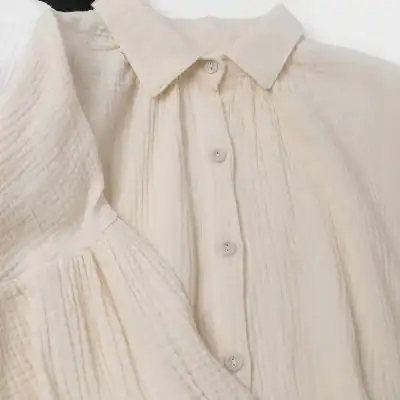 Cream-colored blouse with textured fabric and button-up design, perfect for stylish office wear or casual outings.