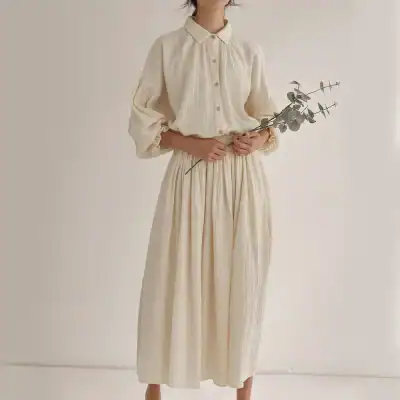 Cream maxi dress featuring pleated fabric, long puff sleeves, and a button-up front, perfect for casual or semi-formal occasions.