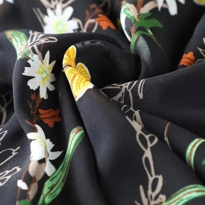 Black fabric with white, yellow, green, and orange floral pattern, perfect for stylish women’s accessories and versatile fashion statements.
