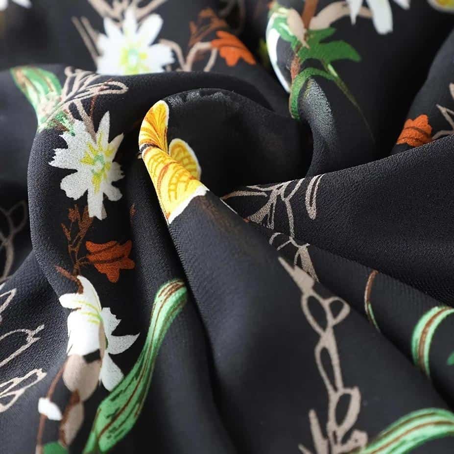 Black fabric with white, yellow, green, and orange floral pattern, perfect for stylish women’s accessories and versatile fashion statements.