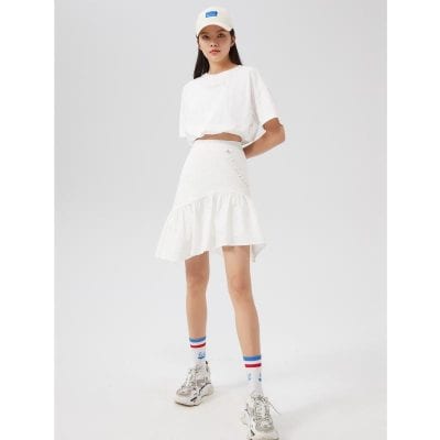 A young woman wearing a trendy white crop top, tiered white skirt, colorful striped socks, and chunky sneakers, showcasing modern street fashion with a sporty and casual look.