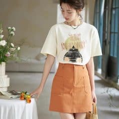 Elegant woman wearing trendy casual outfit with optometry-inspired t-shirt, orange skirt, and accessories, showcasing fashionable eyewear and accessories at Monalisa Store.