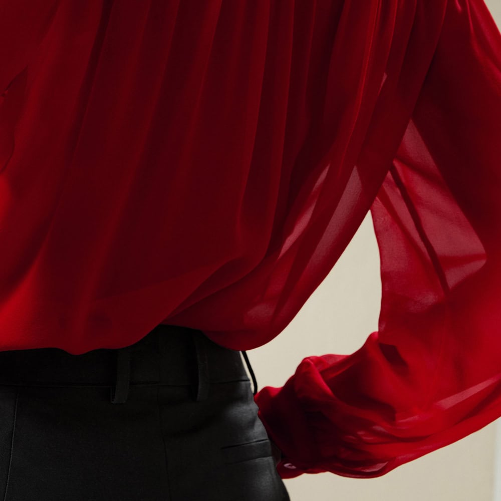 Close-up of a fashionable red women's blouse made of sheer, flowy fabric, paired with black trousers, showcasing stylish and comfortable clothing.