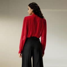 A woman wearing a stylish red blouse with a pleated back design, paired with high-waisted black trousers, showcasing fashionable women's clothing available at Monalisa Store.