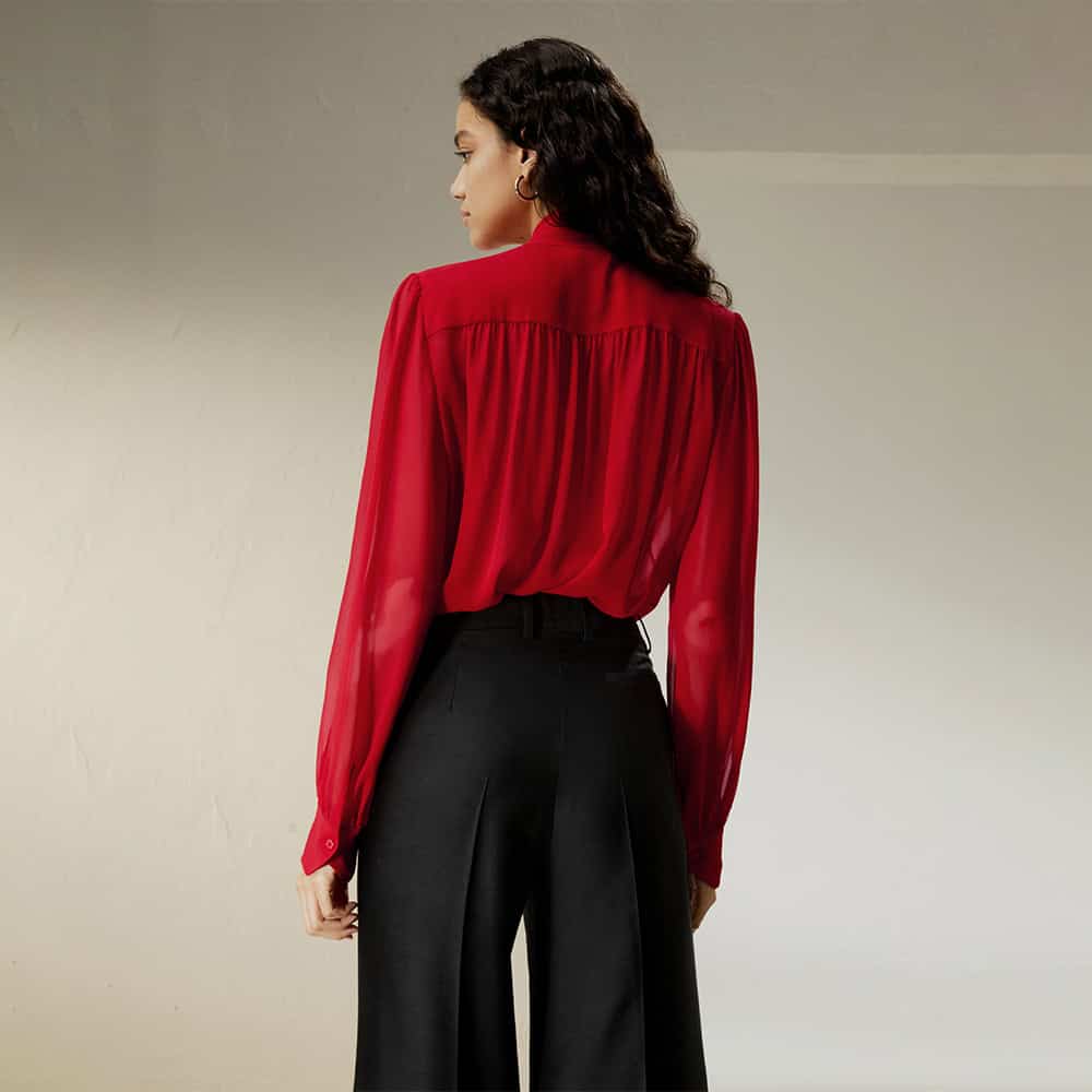 A woman wearing a stylish red blouse with a pleated back design, paired with high-waisted black trousers, showcasing fashionable women's clothing available at Monalisa Store.