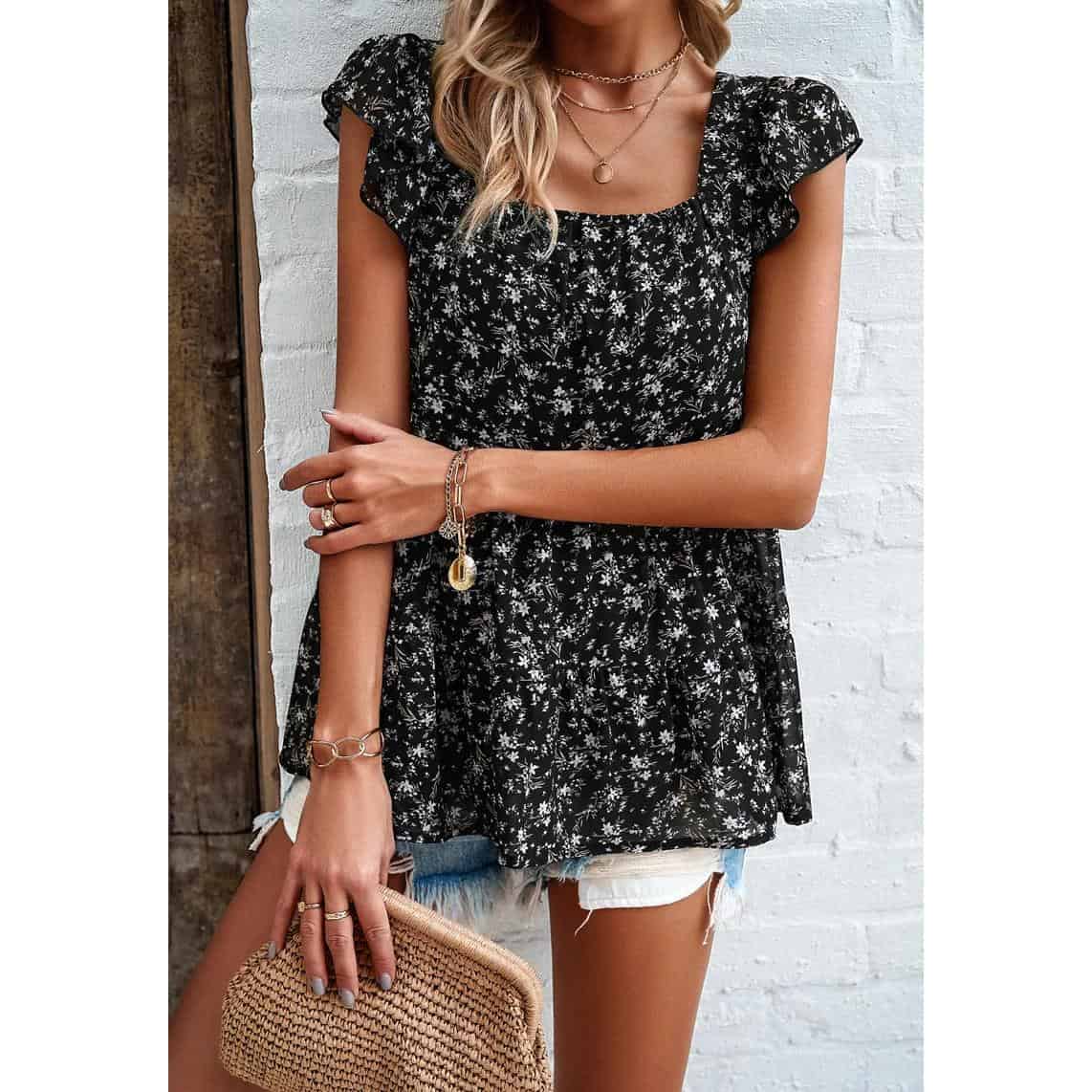 Close-up of a fashionable women’s black floral top, paired with jewelry, denim shorts, and a woven purse, perfect for summer fashion and casual outings.