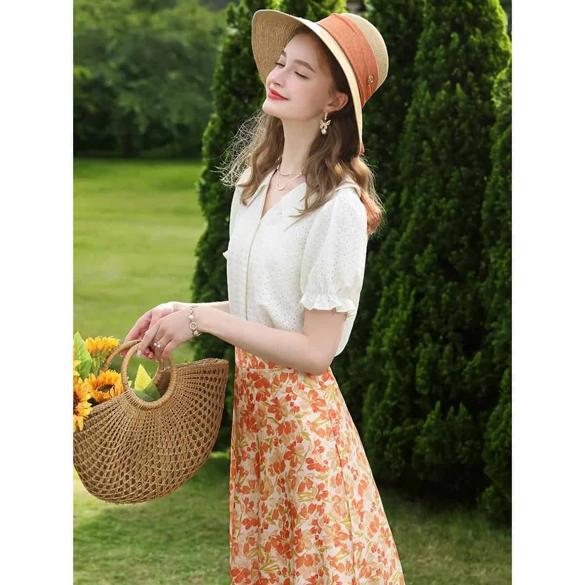 Beautiful woman in summer outfit with floral skirt, white top, straw hat, and wicker basket of flowers, enjoying a sunny day outdoors. Perfect for summer fashion and casual outdoor wear.