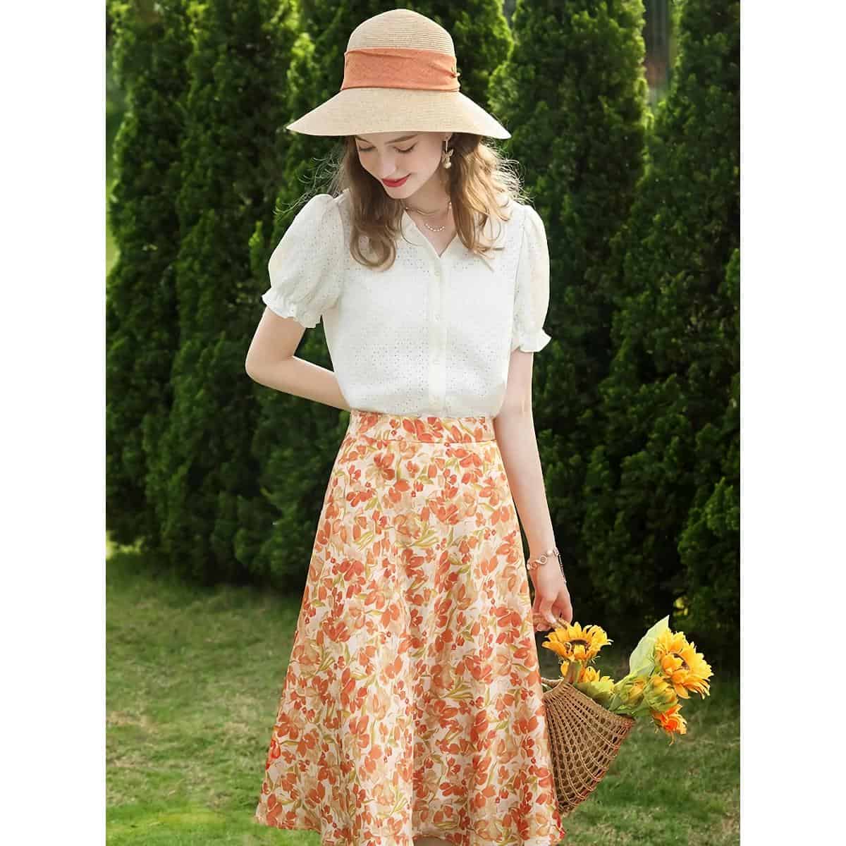 Woman wearing light white blouse and floral wide-leg pants in a garden setting, perfect for summer fashion and opt style.
